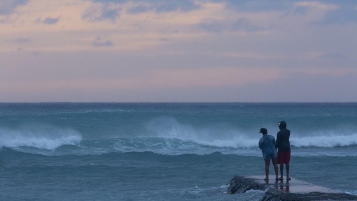HONOLULU, HI - AUGUST 24: Warnings of dangerous rip currents does not deter people from walking the wave swept break wall at the East end of Waikiki beach to take selfies with the sunset and stormy seas caused by Hurricane Lane on August 24, 2018.   Kat Wade/Getty Images/AFP