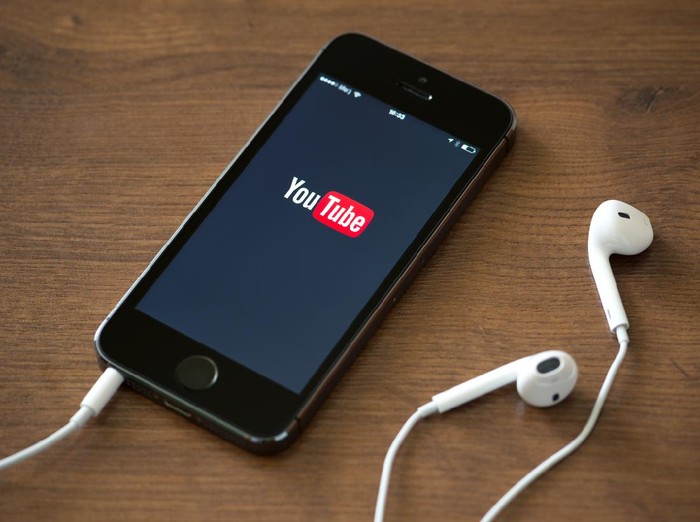 Kiev, Ukraine - June 5, 2014: Brand new Apple iPhone 5S with YouTube application service on the screen lying on a desk with headphones. YouTube is the worlds most popular online video-sharing website that founded in February 14, 2005