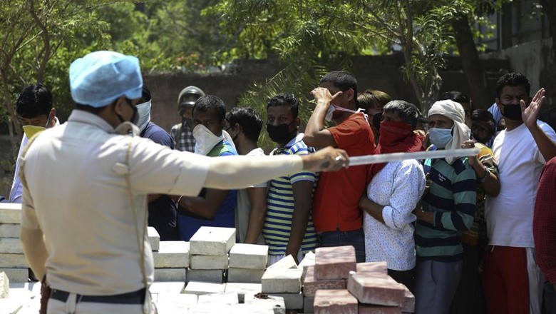 Warga India mengantre beli miras di New Delhi A police personnel gestures to people queueing up to buy alcohol outside a liquor shop after the government eased a nationwide lockdown imposed as a preventive measure against the spread of the COVID-19 coronavirus in New Delhi on May 5, 2020. (Photo by SAJJAD HUSSAIN / AFP)
