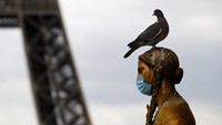 Burung merpati  hinggap di patung yang memakai masker di Lapangan Trocadero, Paris, Prancis (4/5/2020). AP Photo/Christophe Ena.