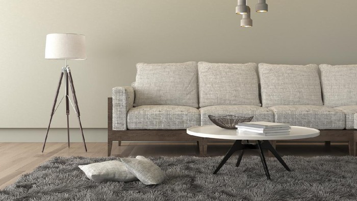 Designer table on brown carpet in front of grey sofa with decorative pillows against tubes in living room