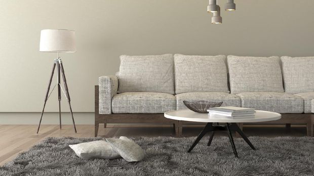 Designer table on brown carpet in front of grey sofa with decorative pillows against tubes in living room