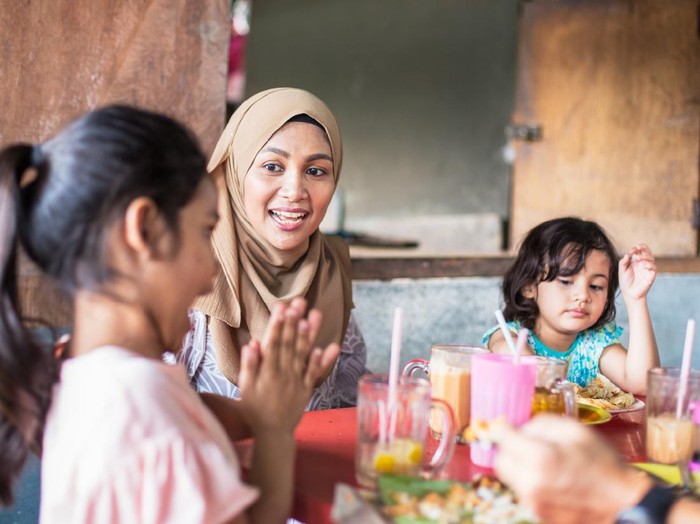 1127348243 Asian family lunch outdoors, children having fun at table, Father helps feed daughter