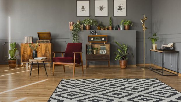 Designer table on brown carpet in front of grey sofa with decorative pillows against tubes in living room