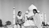 Dua gadis India duduk di kursi taman di pelataran Taj Mahal. Keduanya mengenakan sari, baju khas India yang masih banyak digunakan hingga saat ini. Three Lions/Getty Images.