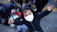 Seorang anak migran dari kamp Moria, Pulau Lesbos, mengenakan masker untuk mencegah penyebaran COVID-19, saat menunggu bus setelah mereka tiba di pelabuhan Piraeus, di Athena, Yunani. 