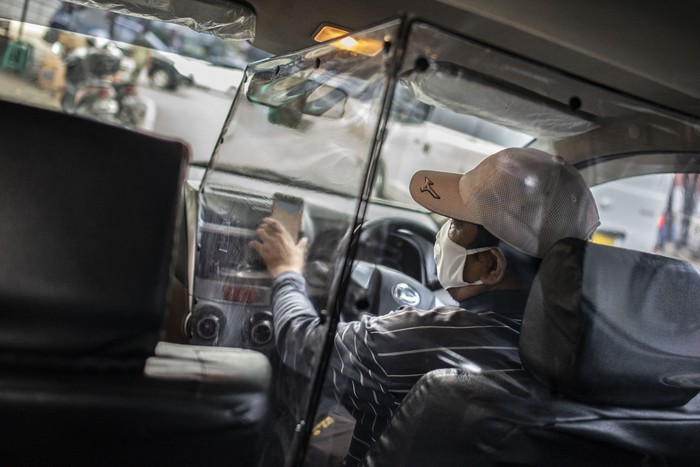 Pengemudi taksi daring, Aris Hardy Halim menunggu calon penumpang di dalam mobilnya yang telah terpasang plastik pembatas di kawasan Bendungan Hilir,  Jakarta, Jumat (8/5/2020). Pemasangan plastik pembatas antara pengemudi dengan penumpang tersebut bertujuan untuk mencegah penyebaran COVID-19 sehingga memberikan kenyamanan dan keamanan kepada pelanggan taksi daring. ANTARA FOTO/Aprillio Akbar/pras.