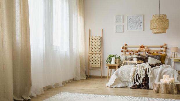 Candles on wood next to bed with knit blanket in hygge style bedroom interior with brown curtain and posters