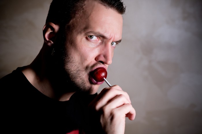 Ilustrasi Lolipop portrait of handsome blond man licking on heart shaped lollipop