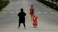 Seorang perempuan menggunakan kostum kelulusan di kampus Universitas Kansas, AS (26/4/2020). Pihak kampus memutuskan tidak mengadakan kelas perkuliahan dan melakukan kuliah jarak jauh (online). AP Photo/Charlie Riedel.