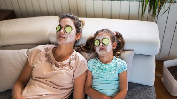 Beautiful mother and daughter with facial mask and slices of cucumber on their eyes enjoying lazy virtual spa day during COVID-19 isolation.