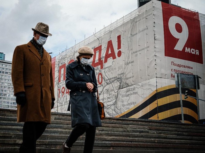 A couple wearing face masks, amid concerns of the COVID-19 coronavirus, walks in front of a huge banner for the upcoming 75th anniversary of the victory over Nazi Germany in World War II that is used to cover a building under renovation in central Moscow on May 7, 2020. (Photo by Dimitar DILKOFF / AFP)
