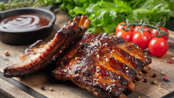 Closeup of pork ribs grilled with BBQ sauce and caramelized in honey. Tasty snack to beer on a wooden Board for filing on dark concrete background.
