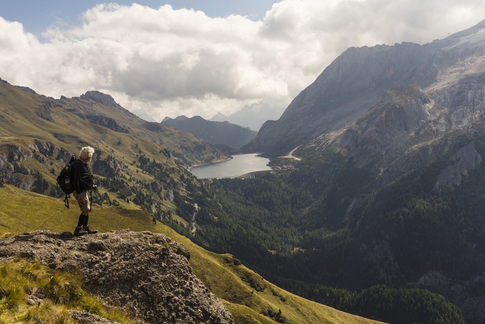 Senior man hiking along hills opposite to the Marmolada in autumn. In distance lake Fedaia. Dolomites, Northern Italy.
