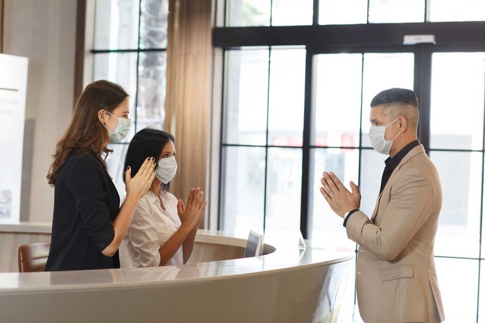 hotel guest and receptionist wearing mask to protect from conronavirus covid 19 having new practice of greeting with thai wai, new greeting practice in coronavirus covid 19 pandemic