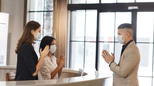 hotel guest and receptionist wearing mask to protect from conronavirus covid 19 having new practice of greeting with thai wai, new greeting practice in coronavirus covid 19 pandemic