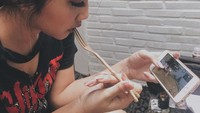 Wah, ternyata Cindy Caroline termasuk gamers. Lihat saja meski sambil makan pun dibarengi dengan main games di handphonenya.  Foto: Instagram @c.eendy
