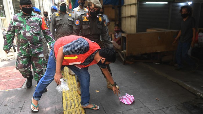 Seorang warga yang terjaring razia penindakan pelanggaran aturan Pembatasan Sosial Berskala Besar (PSBB) oleh Satpol PP menjalani hukuman dengan cara membersihkan sampah di Tanah Abang, Jakarta, Rabu (13/5/2020). Pemprov DKI Jakarta mulai memberlakukan sanksi sosial terhadap pelanggar PSBB yaitu dengan memakaikan rompi bertuliskan pelanggar PSBB saat mereka membersihkan fasilitas umum. ANTARA FOTO/Akbar Nugroho Gumay/aww.