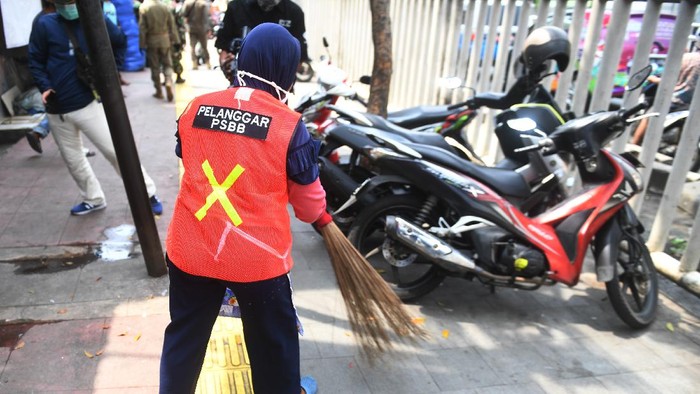 Seorang warga yang terjaring razia penindakan pelanggaran aturan Pembatasan Sosial Berskala Besar (PSBB) oleh Satpol PP menjalani hukuman dengan cara membersihkan sampah di Tanah Abang, Jakarta, Rabu (13/5/2020). Pemprov DKI Jakarta mulai memberlakukan sanksi sosial terhadap pelanggar PSBB yaitu dengan memakaikan rompi bertuliskan pelanggar PSBB saat mereka membersihkan fasilitas umum. ANTARA FOTO/Akbar Nugroho Gumay/aww.