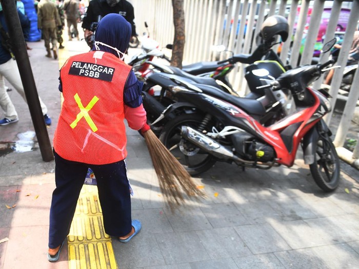 Seorang warga yang terjaring razia penindakan pelanggaran aturan Pembatasan Sosial Berskala Besar (PSBB) oleh Satpol PP menjalani hukuman dengan cara membersihkan sampah di Tanah Abang, Jakarta, Rabu (13/5/2020). Pemprov DKI Jakarta mulai memberlakukan sanksi sosial terhadap pelanggar PSBB yaitu dengan memakaikan rompi bertuliskan pelanggar PSBB saat mereka membersihkan fasilitas umum. ANTARA FOTO/Akbar Nugroho Gumay/aww.