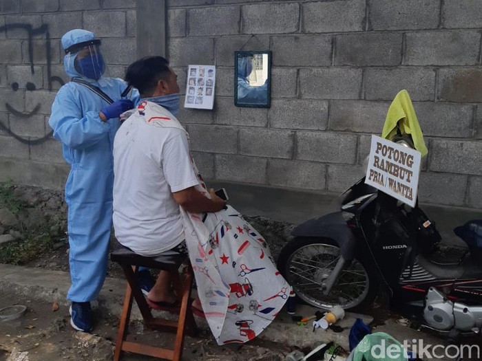 Foto tukang cukur keliling di Surabaya viral di media sosial. Tukang cukur tersebut mencuri perhatian karena menggunakan APD tenaga medis.