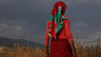 Seorang petani sambil memegang arit berdiri melihat ladang gandum yang akan dipanen.