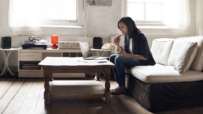 Woman sitting on sofa using laptop in her cozy loft apartment