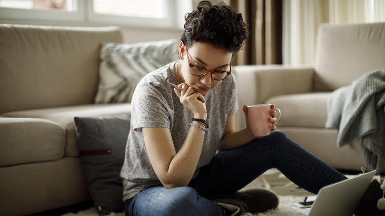 457207791 Woman sitting on sofa using laptop in her cozy loft apartment