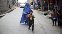 Anak kecil membawa roti di depan perempuan berburqa, di Kabul, Afghanistan (5/5/2020).  AP Photo/Rahmat Gul