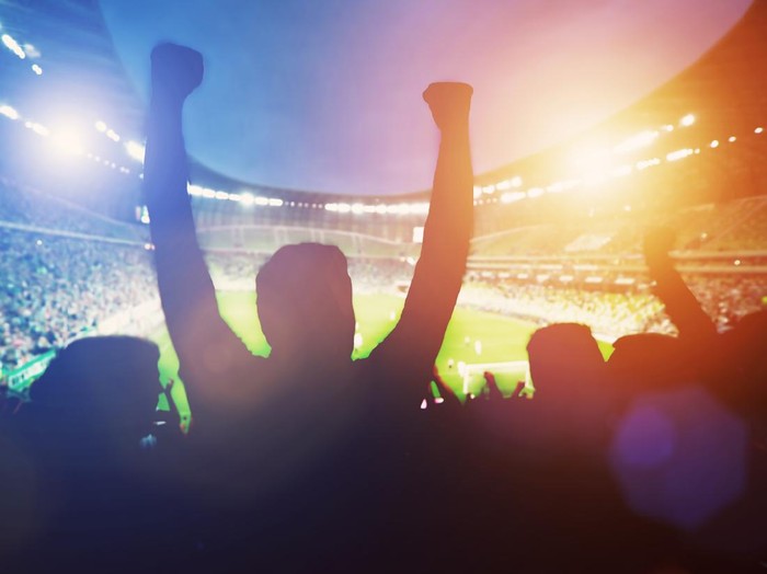 Happy football fans support their team and celebrating goal with hands up. Big stadium