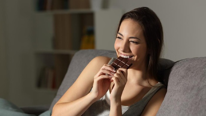 Woman enjoying eating chocolate in the night sitting on a couch in the living room at home