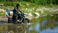 Seorang Bintara Pembina Desa (Babinsa) Kopral Satu (Koptu) Ishak Nur mengendarai motor yang telah dipasang kotak makanan melintasi sungai menuju desa terpencil Ayuhula, Kabupaten Gorontalo, Gorontalo, Sabtu (16/5/2020) kemarin.