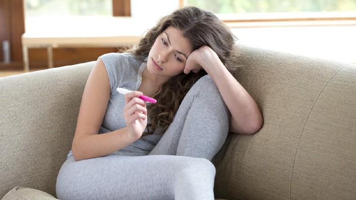 503117013 Young woman looking miserable staring at pregnancy test