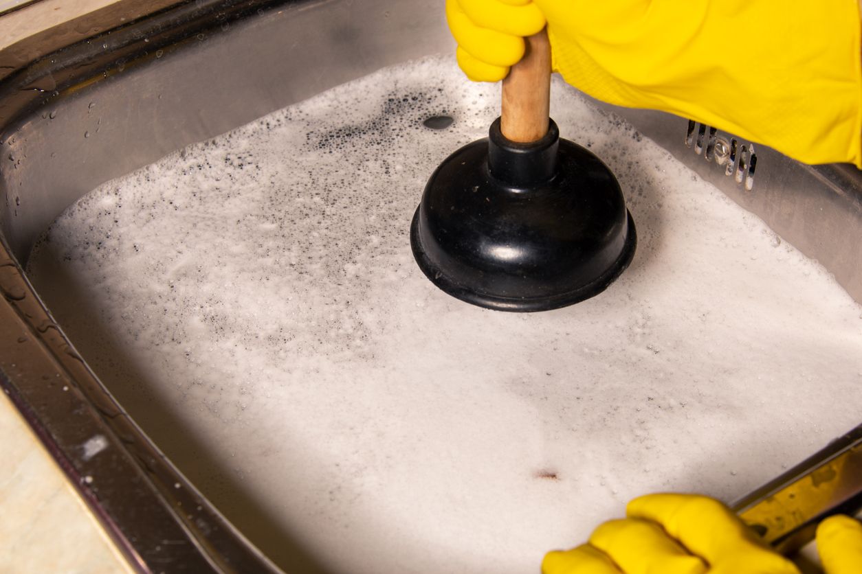 Concept of how to fix blockages with a plunger. Clogged pipes and sink in the kitchen.