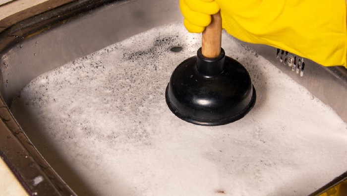 Concept of how to fix blockages with a plunger. Clogged pipes and sink in the kitchen.
