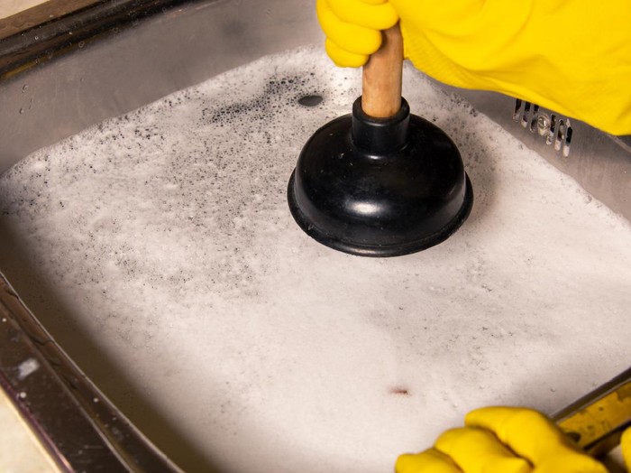 Concept of how to fix blockages with a plunger. Clogged pipes and sink in the kitchen.