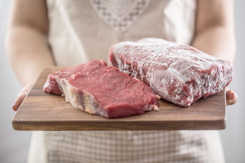 Female cook holding wooden board of raw and frozen beef  meat.