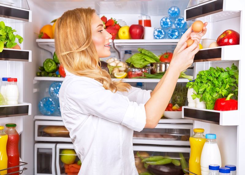Cute female taking eggs from the fridge, attractive housewife take care about health, fresh tasty organic food, healthy eating concept