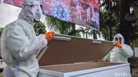 Petugas mengenakan baju hazmat dengan membawa peti mati standard jenazah korban COVID-19.