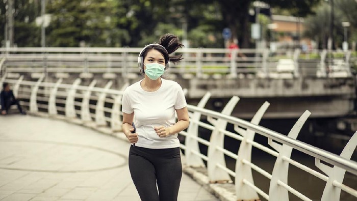 joging jogging lari pakai masker Beautiful female jogger putting protective mask on her face to protect herself from virus or allergy infection. Sunset in background.