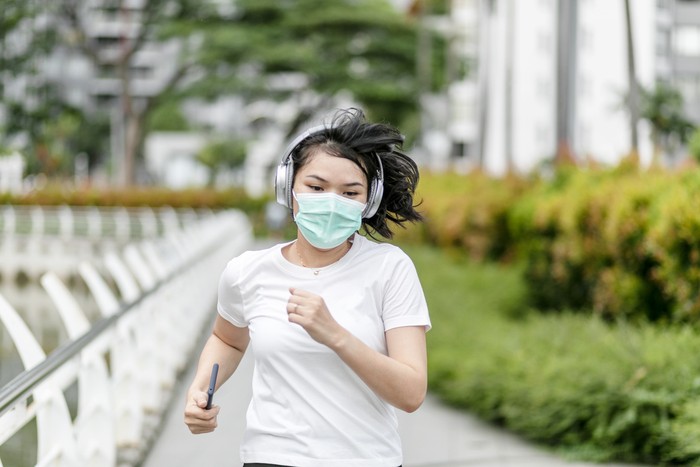 joging jogging lari pakai masker Beautiful female jogger putting protective mask on her face to protect herself from virus or allergy infection. Sunset in background.