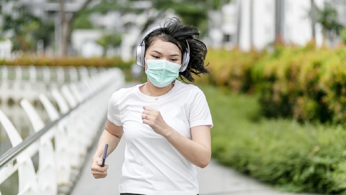 Beautiful female jogger putting protective mask on her face to protect herself from virus or allergy infection. Sunset in background.