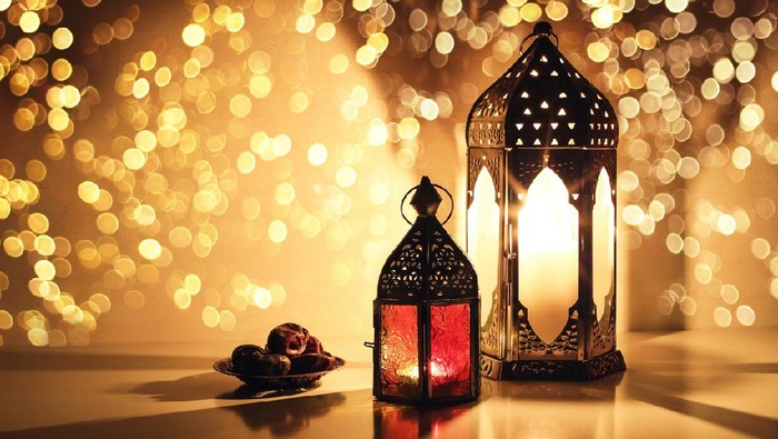 Ornamental Arabic lanterns with burning candles. Glittering golden bokeh lights. Plate with date fruit on the table. Greeting card for Muslim holiday Ramadan Kareem, iftar dinner background.