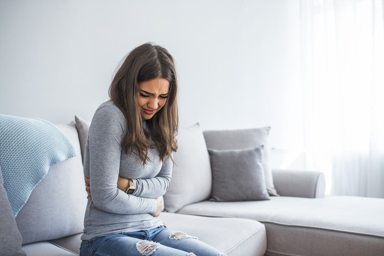 Woman lying on sofa looking sick in the living room. Beautiful young woman lying on bed and holding hands on her stomach. Woman having painful stomachache on bed, Menstrual period