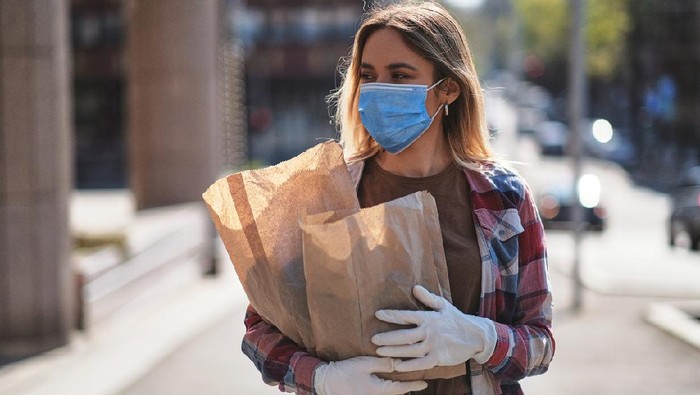 Young women wearing protective face mask and protective gloves to prevent Corona virus and other diseases, going home afrer shopping groceries, Covid-19 outbreak