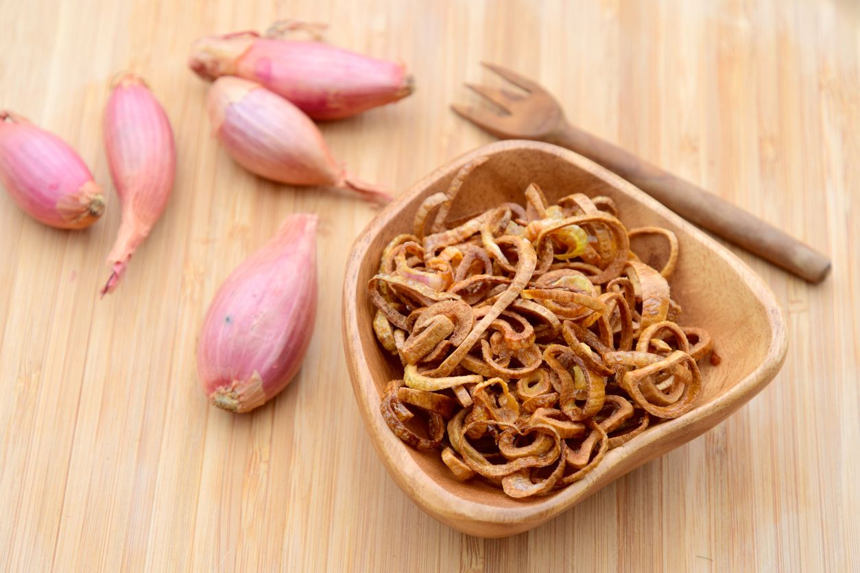 crispy fried shallot (bawang goreng) in wooden bowl over wooden background.