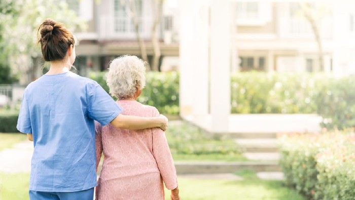 Back view of nurse caregiver support walking with elderly woman outdoor
