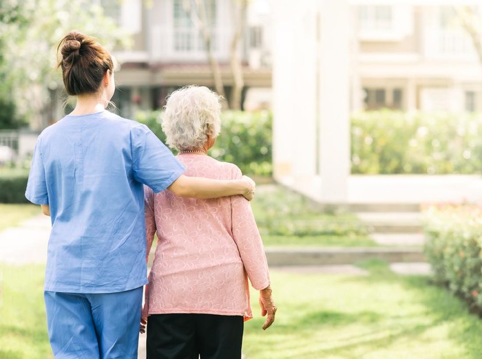 Back view of nurse caregiver support walking with elderly woman outdoor