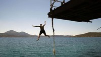 Anak laki-laki melompat ke laut di pulau Laut Milos pada Minggu (24/05) menyongsong musim turis asing pada 15 Juni 2020 mendatang. (Thanassis Stavrakis/AP) 
