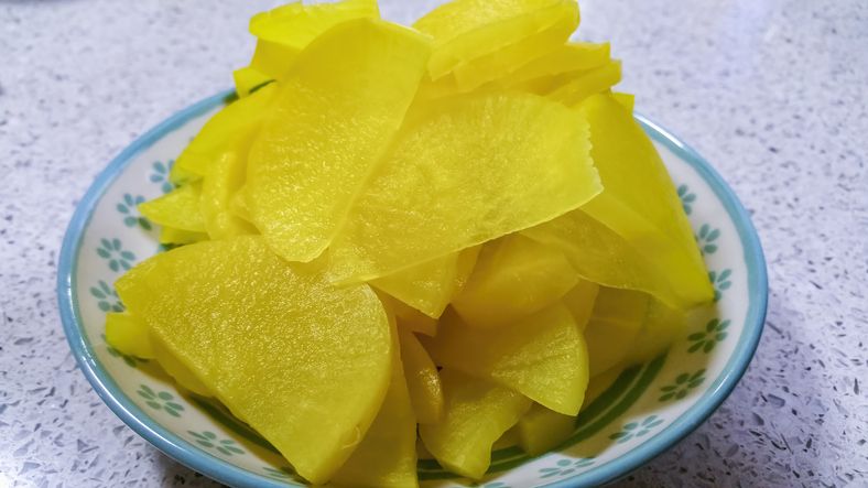 Slices of yellow pickled daikon radish served on a plate. A healthy accompaniment to Japanese and Korean foods.